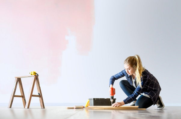 Alt-text: Mladá žena pracuje s vrtačkou na kusu dřeva v čerstvě zrenovované místnosti.