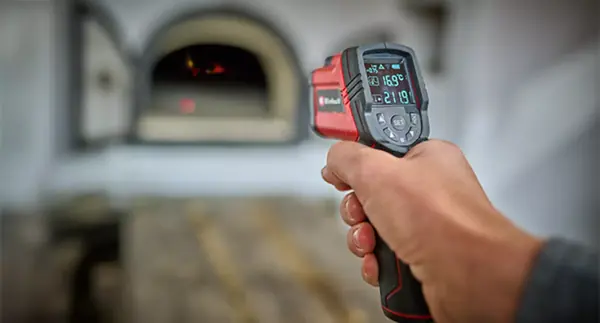 Ruka používá infračervený teploměr Einhell TC-IT 550 k měření teploty u otvoru trouby.