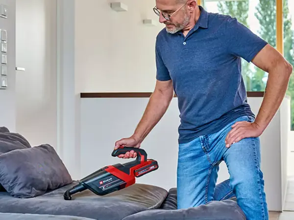 Muž vysává pohovku akumulátorovým ručním vysavačem Einhell TE-HV 18/06 Li.