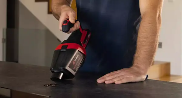 Akumulátorový ruční vysavač Einhell TE-HV 18/06 Li vysává kávová zrna na stole.