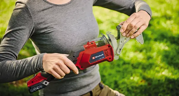 Osoba demontuje držák větví z akumulátorové prořezávací pily Einhell GE-GS 18/150 Li-Solo. Držák je odnímatelný.