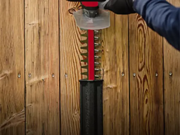 Akumulátorové nůžky na živý plot Einhell GC-CH 18/50 Li-Solo zavěšené svisle v nástěnném držáku na dřevěné stěně.