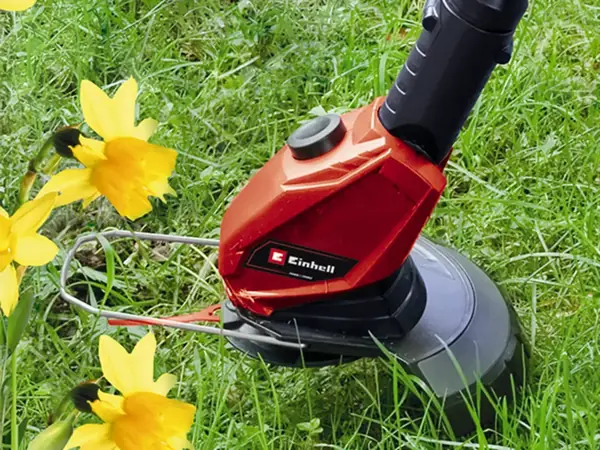 Der Einhell Akku-Rasentrimmer GE-CT 18 Li-Solo im Einsatz, schneidet Gras um gelbe Blumen im Garten.