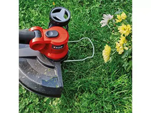 Střihací hlava aku vyžínače Einhell GE-CT 18/30 Li-Solo s cívkou struny a ochranným krytem v blízkosti žlutých květin.