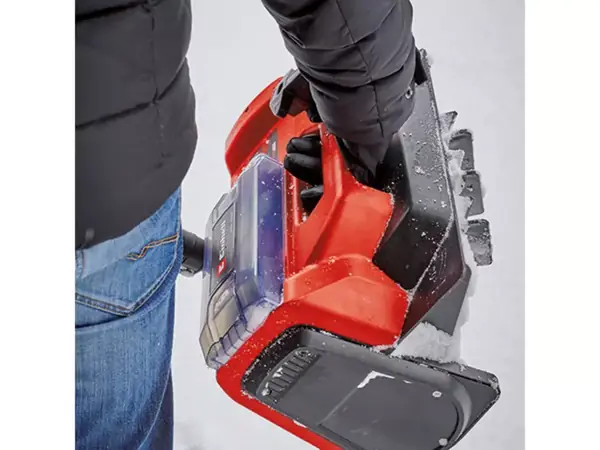 Osoba nese sněhovou frézu za integrované madlo.