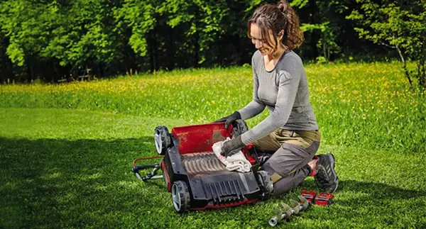 Žena klečí na trávníku a čistí aku vertikutátor-provzdušňovač Einhell GE-SC 36/35 Li-Solo hadříkem, vedle něj leží váleček.