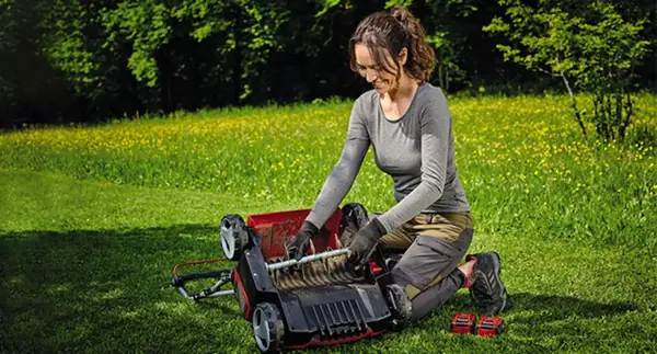 Žena klečí na trávníku a sundává válec z převráceného aku vertikutátoru Einhell GE-SC 36/35 Li-Solo.
