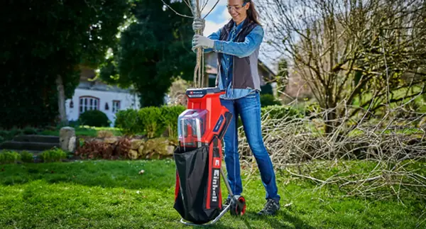 Žena obsluhuje akumulátorový nožový drtič REDAXXO 36/25 na zahradě a vkládá větve do horního plnicího otvoru.