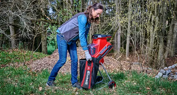 Žena sahá na sběrný vak akumulátorového nožového drtiče REDAXXO 36/25 na zahradě.
