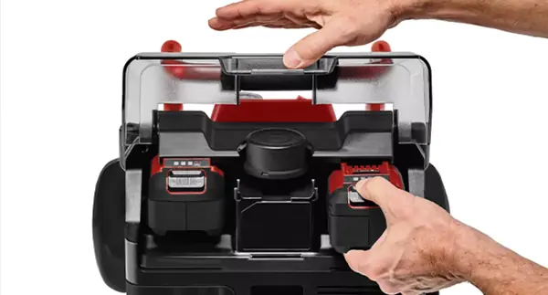 Zwei Hände setzen einen zweiten Akku unter einer transparenten Schutzabdeckung in den Akku-Kompressor ein.