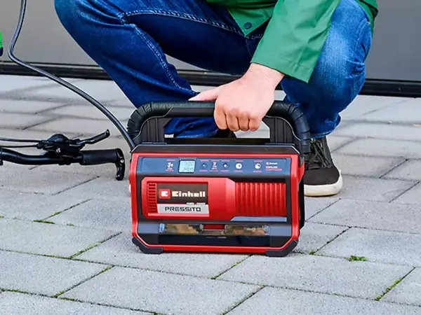 Muž ovládá akumulátorový kompresor Einhell PRESSITO 18/25 na dlážděném povrchu.