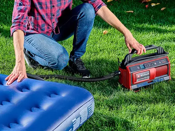 Osoba používá akumulátorový kompresor Einhell PRESSITO 18/25 k nafouknutí matrace na zahradě.