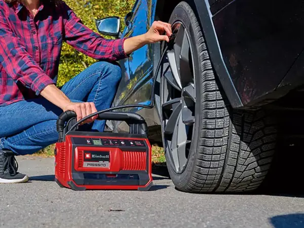 Osoba pumpuje pomocí akumulátorového kompresoru Einhell PRESSITO 18/25 pneumatiku automobilu.