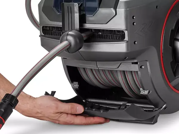 Ruka otevírá údržbovou klapku bezdrátového hadicového navijáku Einhell GE-HR 18/30-1 Li pro snadné čištění.