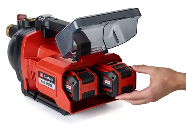 Dva sloty pro akumulátory s otevřeným krytem na zahradním čerpadle Einhell AQUINNA 36/30; ruka vkládá akumulátor.