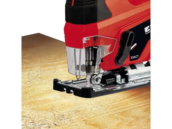 Pohled zepředu na akumulátorovou přímočarou pilu Einhell TC-JS 18 Li při řezání dřevěné desky; funkce odfukování prachu udržuje řezací linii čistou.