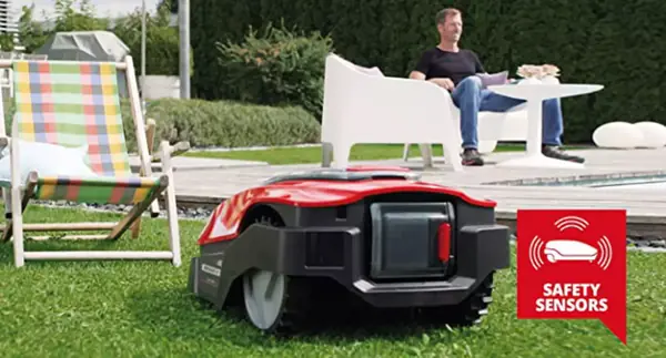 Robotická sekačka Einhell FREELEXO jede po trávníku, zatímco muž sedí na terase; vpravo dole je vidět symbol „SAFETY SENSORS“
