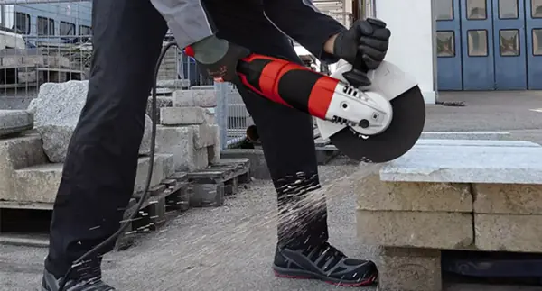 Úhlová bruska Einhell TE-AG 230/2000 se používá venku k řezání kamenných desek, s viditelnými jiskrami.