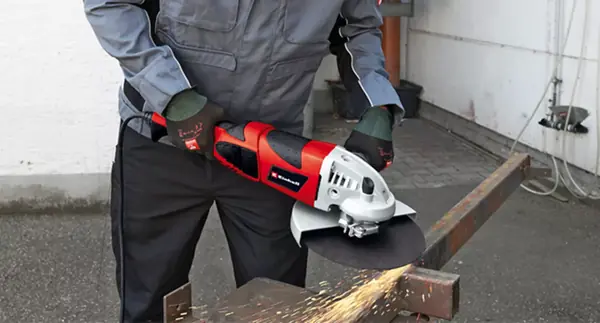 Úhlová bruska Einhell TE-AG 230/2000 v akci při řezání kovového nosníku na dvoře, s viditelnými jiskrami.