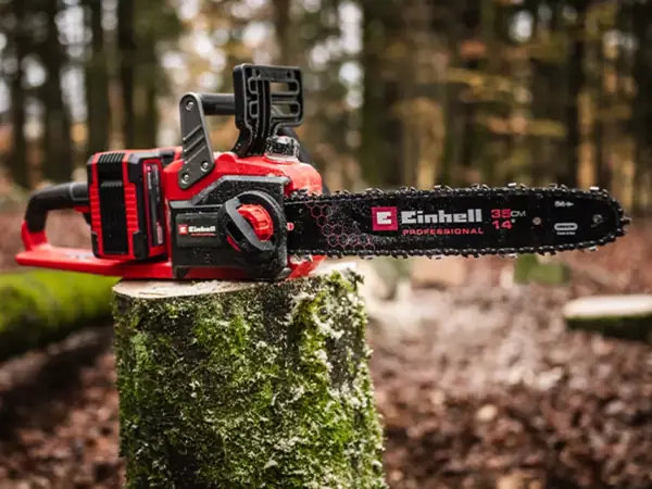 Osoba pracuje s akumulátorovou řetězovou pilou na ležícím kmeni.