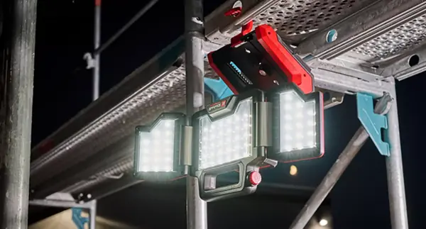 Akumulátorová lampa Einhell TP-CL 18/3000 Li - Solo svítí ve tmě a je hlavou dolů zavěšená na stavebním lešení. Všechny tři LED plochy jsou zapnuté.