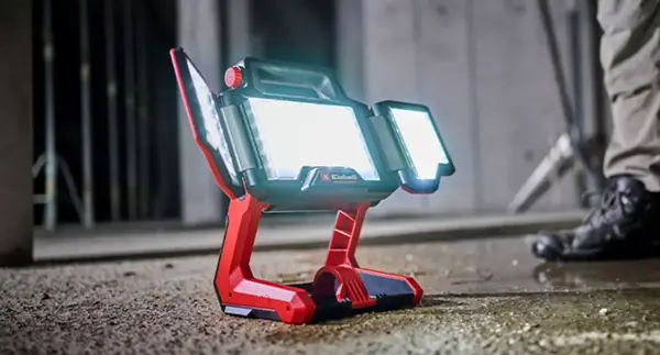 Akumulátorová lampa Einhell TP-CL 18/3000 Li - Solo stojí zapnutá na podlaze staveniště. Všechny tři LED panely svítí jasně.