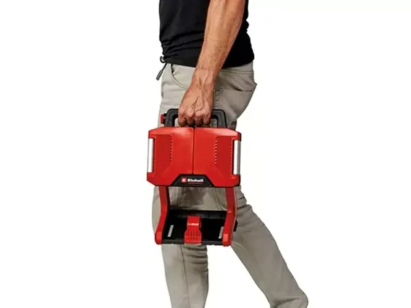 Osoba nese akumulátorovou lampu Einhell TP-CL 18/3000 Li - Solo za rukojeť v pravé ruce. Lampa má rukojeť pro přenášení.