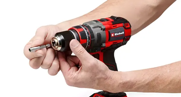 Dvě ruce zasouvají vrták do kovového sklíčidla akumulátorového příklepového šroubováku Einhell.
