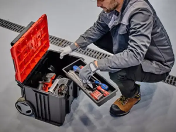 Muž ukládá nářadí do otevřeného kufru Einhell E-Case L with wheels na stavbě.