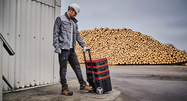 Muž táhne stoh kufrů Einhell E-Case L with wheels po průmyslovém areálu za sebou.