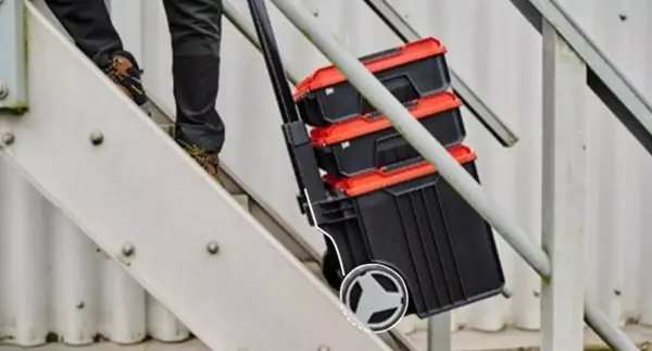 Muž nese stoh kufrů Einhell E-Case L with wheels po schodech nahoru.