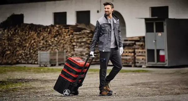 Muž táhne kufr Einhell E-Case L with wheels po nezpevněném terénu.