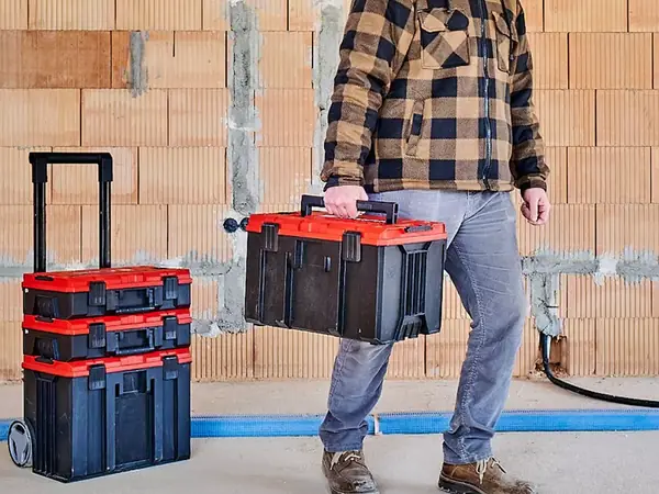 Osoba nese systémový kufr Einhell E-Case M samostatně, v pozadí jsou další kufry.