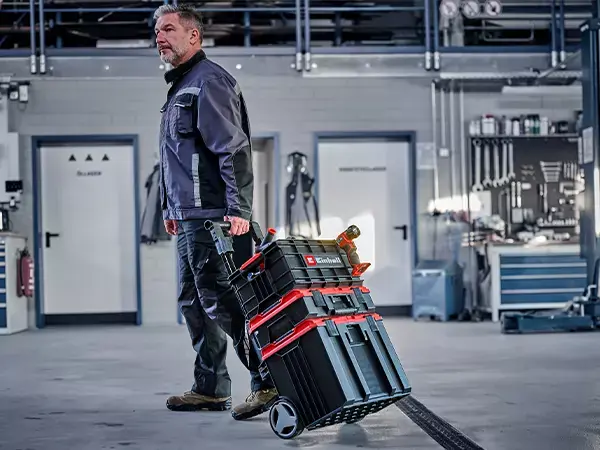 Muž táhne nářaďový kufr Einhell E-Case jako součást stohované věže na kolečkách.