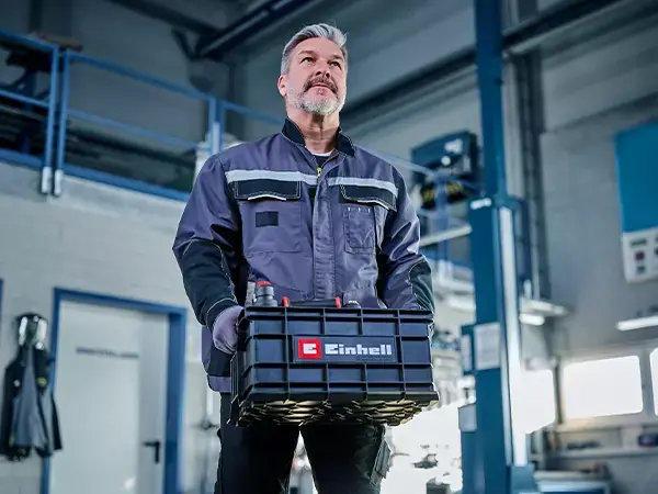 Muž nese nářaďový kufr Einhell E-Case se dvěma červenými madly před tělem.