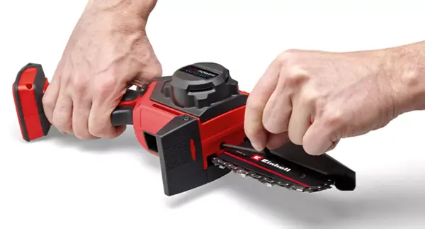 Osoba seřizuje napnutí řetězu akumulátorové prořezávací pily Einhell GE-PS 18/15 Li BL pomocí imbusového klíče.