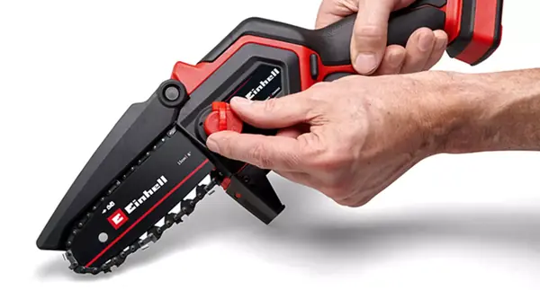 Osoba drží akumulátorovou prořezávací pilu Einhell GE-PS 18/15 Li BL a otáčí červeným napínacím kolečkem pro uvolnění řetězu a lišty.